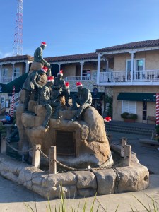 A bunch of statue guys sitting on a rock with their Santa hats on.